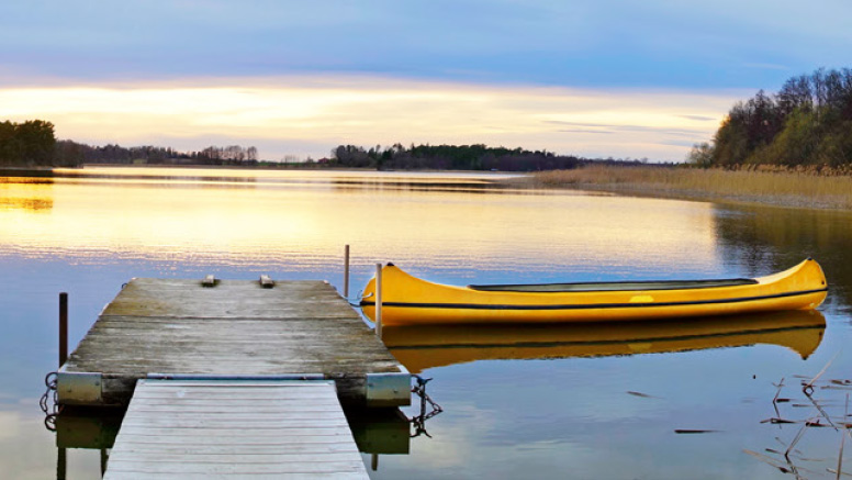 Tranquil scene of sunset, lake, and dock with canoe