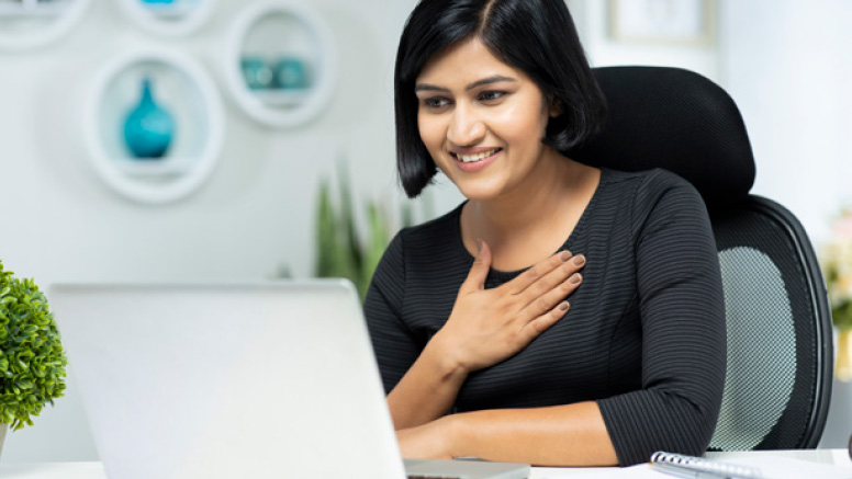 Woman in front of laptop, smiling and holding right hand on chest