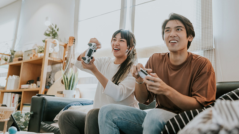 Couple sitting on couch, smiling and holding Nintendo video game controllers