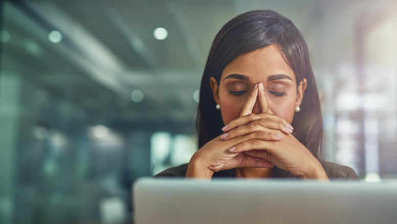 Woman with index fingers on forehead, and hands clasped over face feeling stressed at laptop