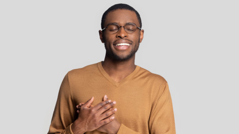 Man smiling, with eyes closed and hands over heart