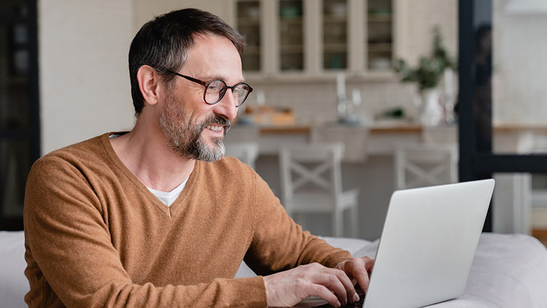 Middle-aged man smiling at home in front of his laptop