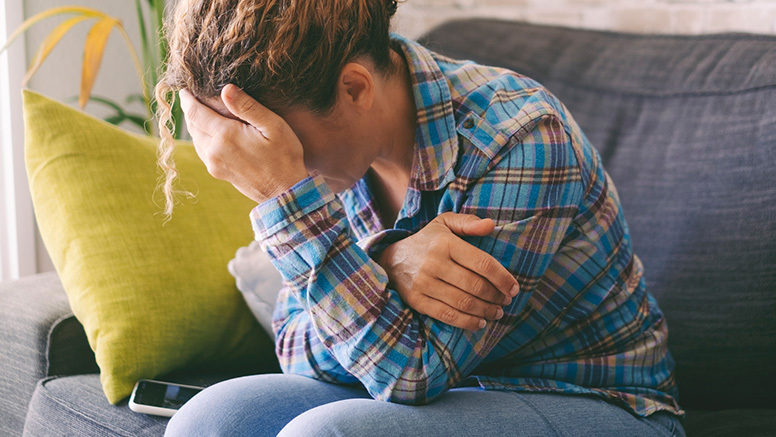 Woman on couch with head in hand signifying financial abuse