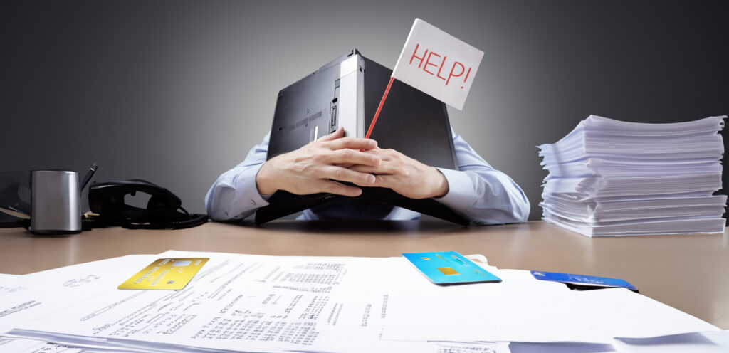 man with head on desk buried under a computer looking for debt help
