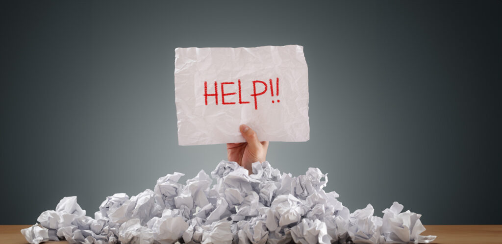 Someone holding a HELP sign under a pile of wadded-up bills
