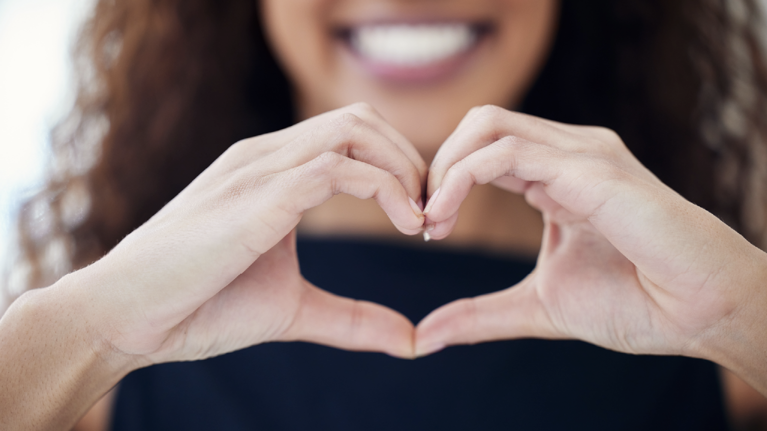 Closeup of woman smiling with her hands making a heart demonstrating Beyond Finance clients appreciating success