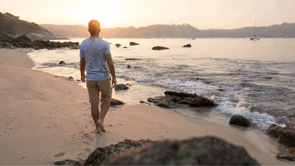 Photo of man walking on rocky beach at sunset