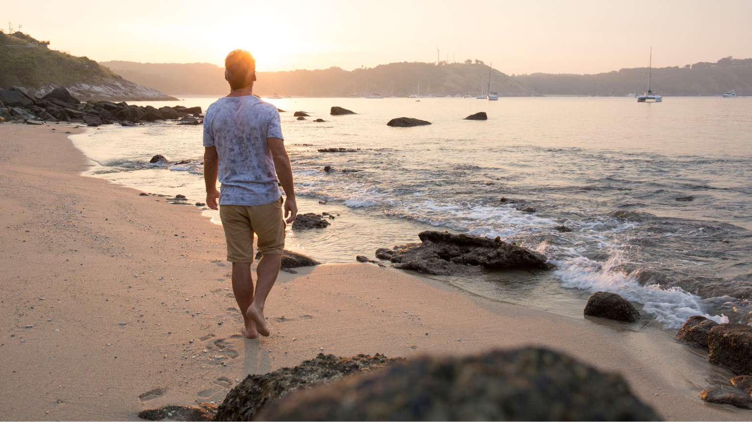 Photo of man walking on rocky beach at sunset